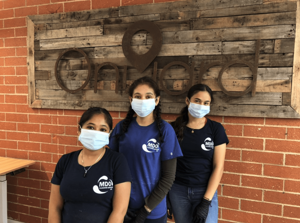 Three women wearing masks standing in front of a brick wall.